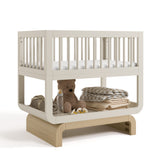 Santorini frosted oat with driftwood bassinet angle view with baby items on bottom