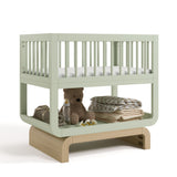 Santorini sage with driftwood bassinet angle view with baby items on bottom