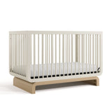 Baby crib in two-tone colorway, at an angled view (Frosted Oat with Driftwood)