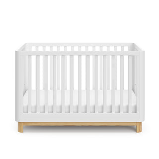 Front view of a white crib with a natural wood color base