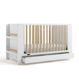 Two-tone white and natural wood baby crib with an open drawer and bookshelf sides