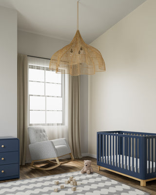 Rocker chair with natural wood base and salt-and-pepper boucle fabric, accompanied by a blue crib with a natural base and a matching blue dresser featuring driftwood knobs, all in a nursery setting.