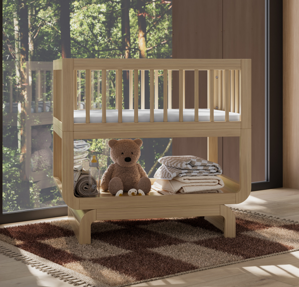 Light natural wood baby bassinet with various children's items, on top of checkered rug