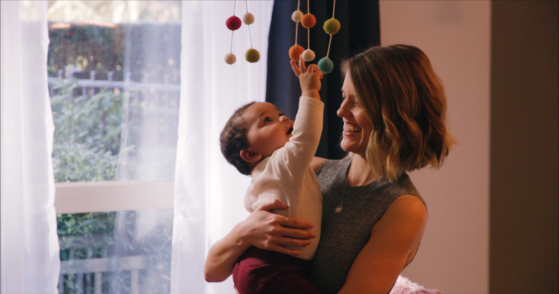 Woman holding baby in her arms as baby reaches for hanging mobile above