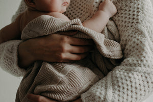 Baby wrapped in knit blanket being held by parent, close to parent's body