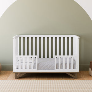 white crib in toddler bed conversion with two toddler safety guardrails, in nursery