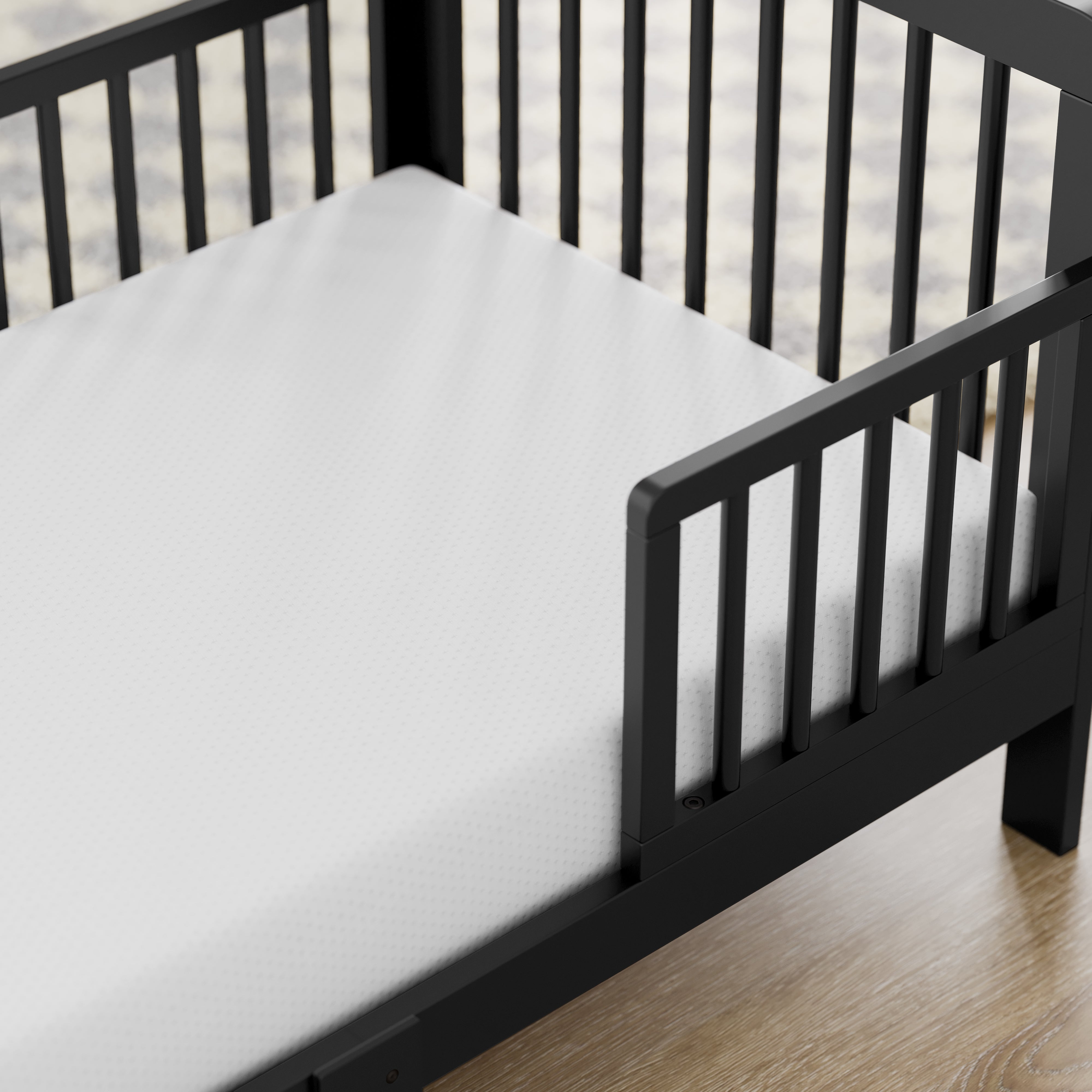storkcraft pasadena black toddler bed closeup of guardrail and headboard on wood floor
