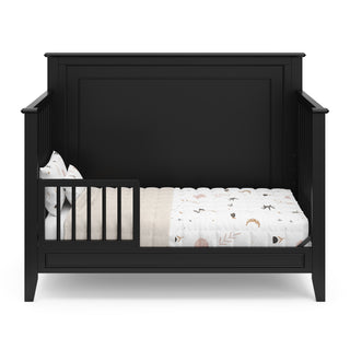 black crib in toddler bed conversion with one toddler safety guardrail