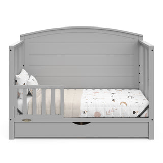 Convertible pebble gray crib transformed into a toddler bed with one guardrails