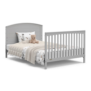  Convertible pebble gray crib transformed into a bed with headboard and footboard.