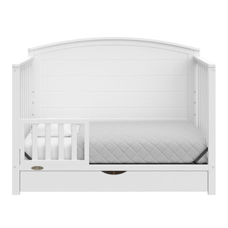 Convertible white crib transformed into a toddler bed with one guardrails
