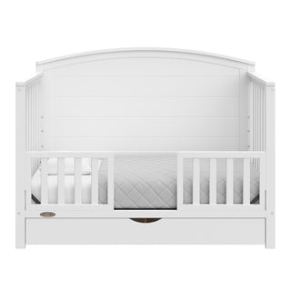 Convertible white crib transformed into a toddler bed with two guardrails