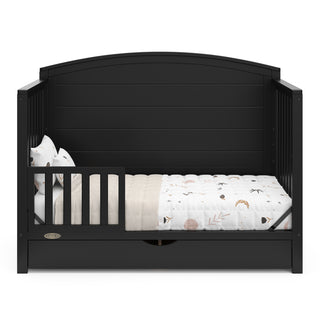 Convertible black crib transformed into a toddler bed with one guardrails