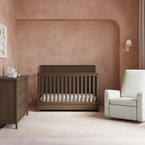 Sasha hazelnut crib with drawer in nursery next to dresser and glider