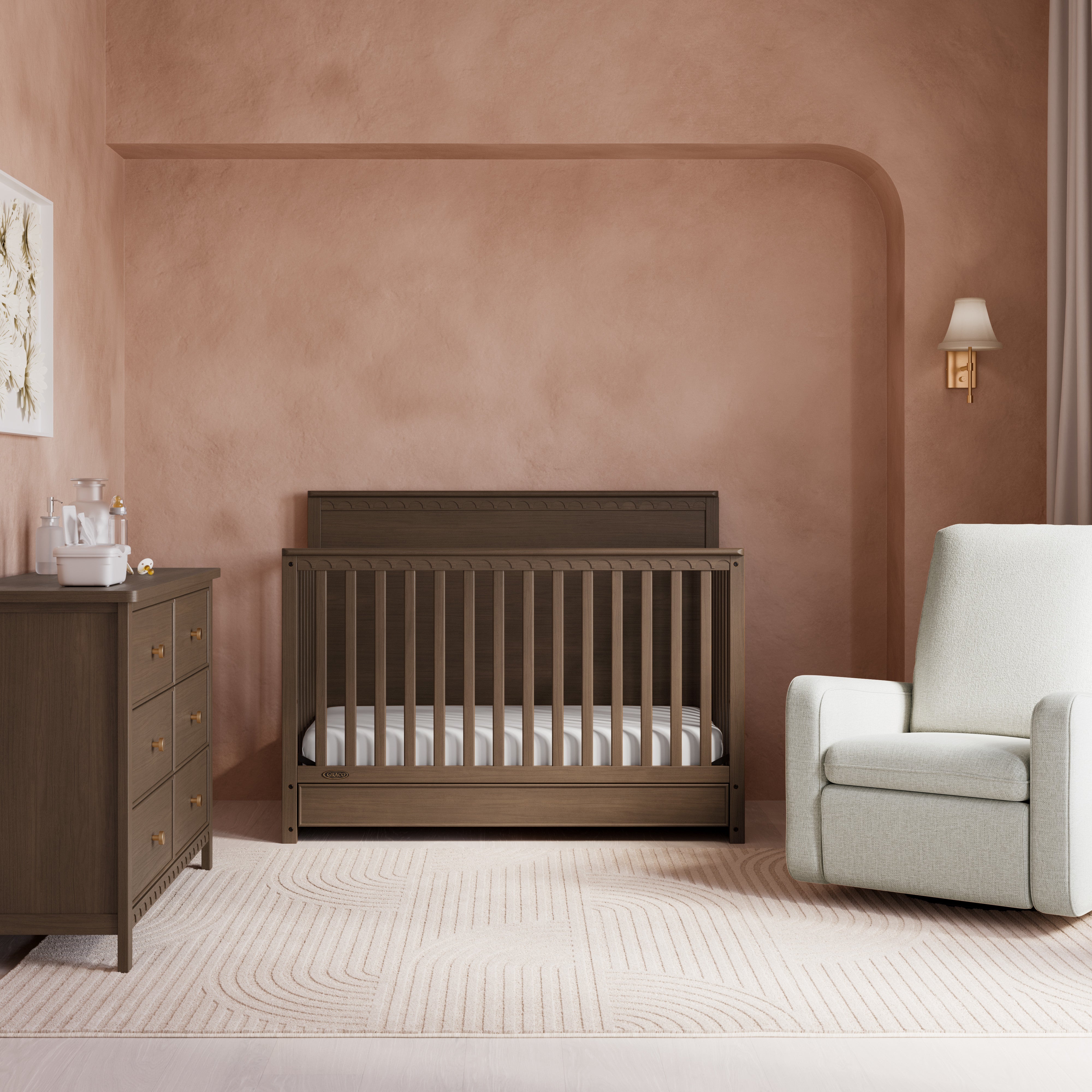 Sasha hazelnut crib with drawer in nursery next to dresser and glider