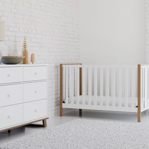 A serene nursery featuring a white and vintage driftwood crib accompanied by a matching 6-drawer dresser.