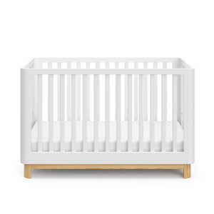 Front view of a white crib with a natural wood color base