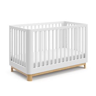 Angled view of a white crib with a natural wood color base