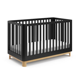 Angled view of a black crib with a natural wood color base