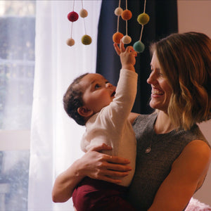 Woman holding baby in her arms as baby reaches for hanging mobile above