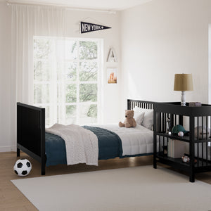 Black bed in kids bedroom setting with matching black nightstand, with various decorative kids bedroom objects including a lamp and soccer ball