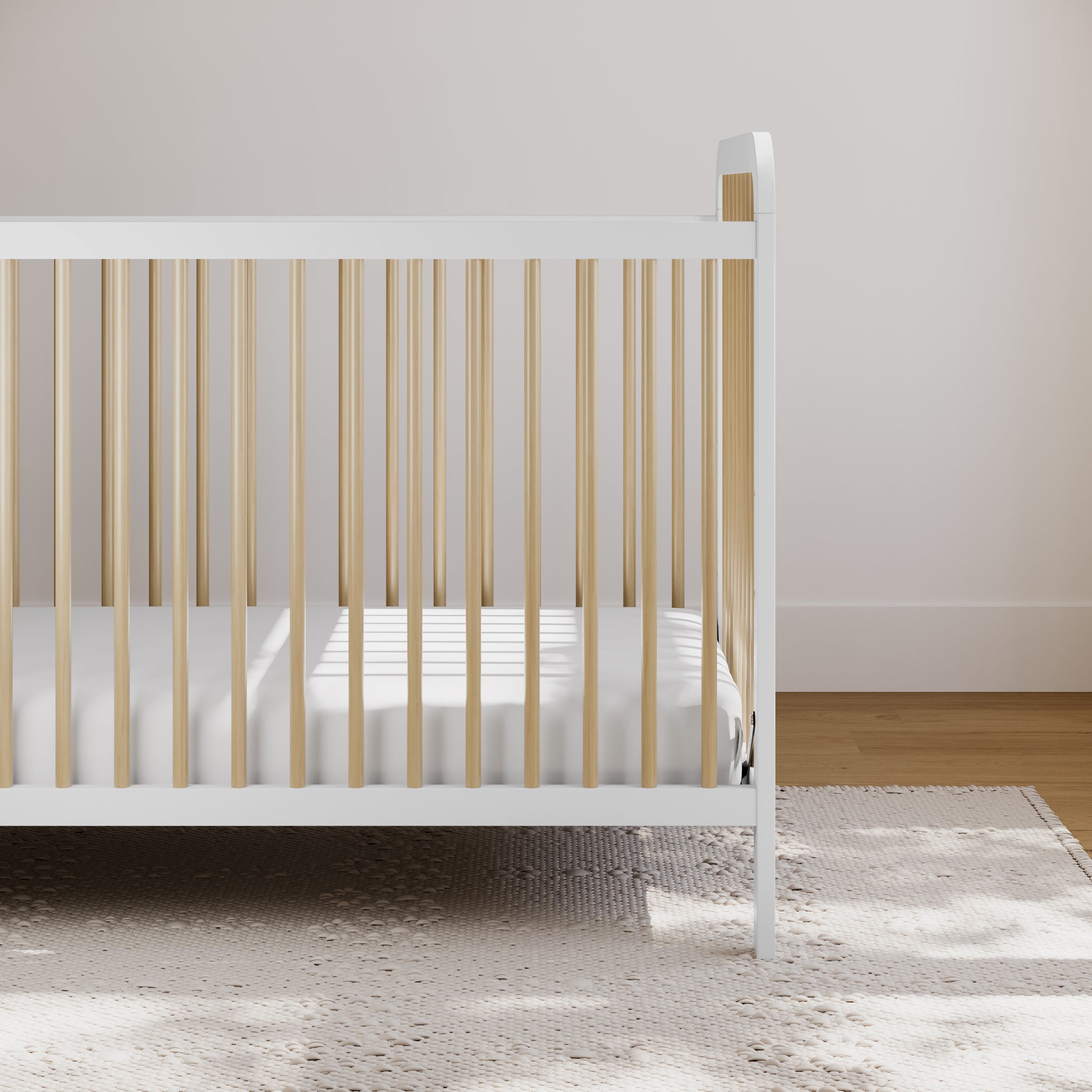 White baby crib with natural wood dowels in nursery bedroom setting on beige rug