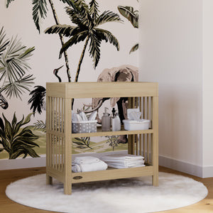 Baby changing table in natural wood color against safari themed wallpaper, outfitted with various nursery accessories