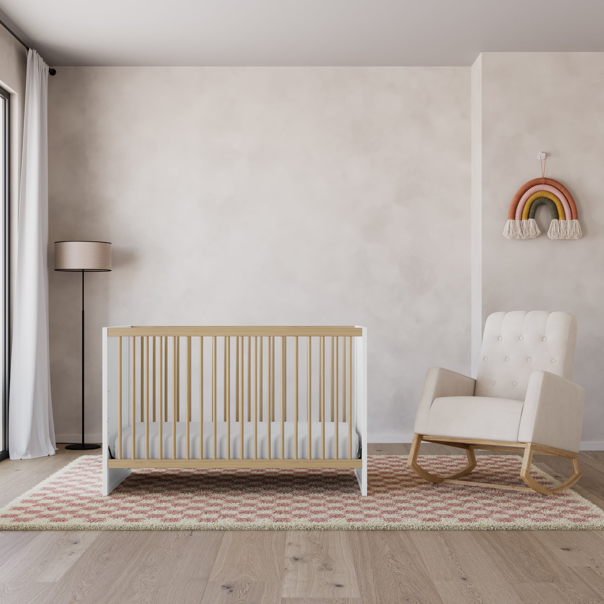 Two-tone white with natural wood baby crib, next to beige nursery rocking chair with natural wood base, in bedroom setting, surrounded by various decorative objects like a checkered rug, a lamp, and a hanging rainbow on the wall behind the chair