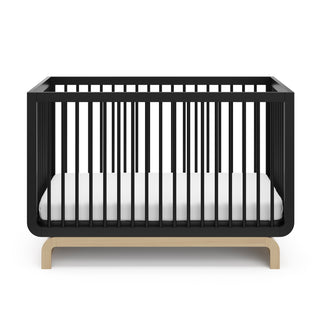 Two-tone black and natural wood baby crib, at a front-facing angle