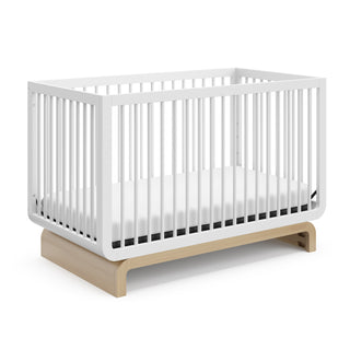 Baby crib in two-tone white and natural wood colorway, at an angle