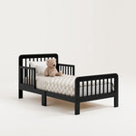 storkcraft pasadena black toddler bed studio angle view with checkered bedding and teddy bear