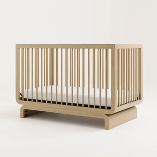 Baby crib in natural wood color, situated at an angle in a studio setting