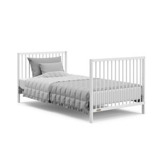 white mini crib in full-size bed with headboard and footboard