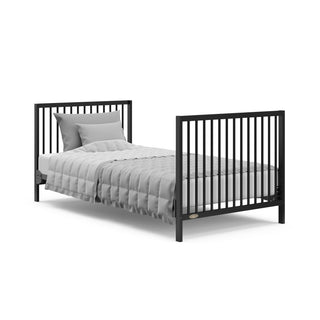 black mini crib in full-size bed with headboard and footboard