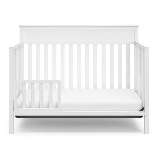 White crib in toddler bed conversion with one safety guardrail