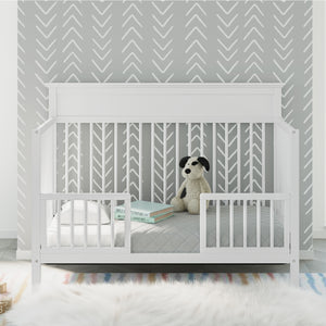 White crib in toddler bed conversion with guardrails, in nursery