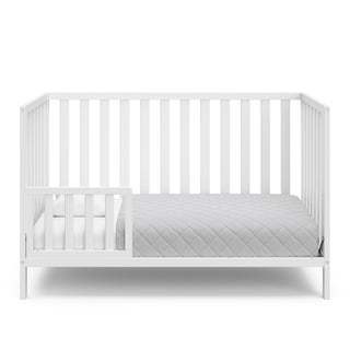 White crib in toddler bed conversion with one safety guardrail