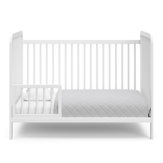 White crib in toddler bed conversion with one safety guardrail 