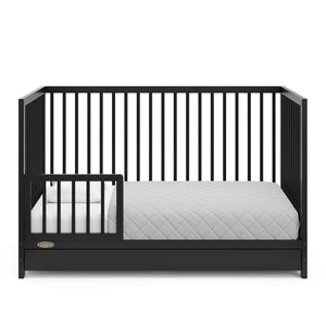 Black crib with drawer in toddler bed conversion with one safety guardrail