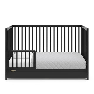 Black crib with drawer in toddler bed conversion with one safety guardrail