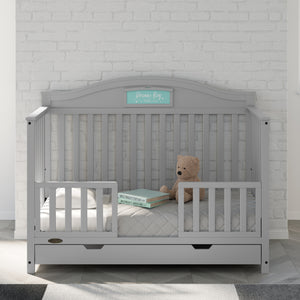 Pebble gray crib with toddler safety guardrails in nursery