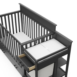 Close-up view of gray crib and changer with open drawer