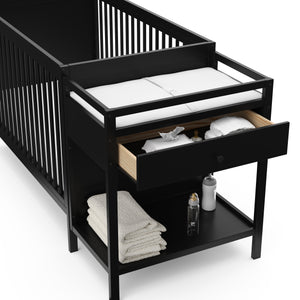 Close-up view of black crib and changer with open drawer
