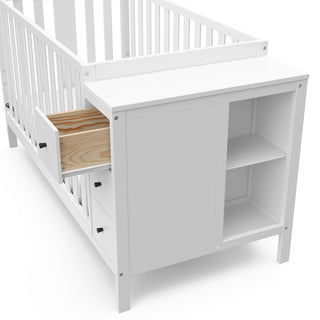 Close-up view of white crib with storage and open drawer