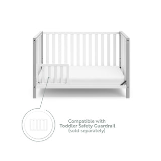 White crib with pebble gray in toddler bed conversion with one safety guardrail graphic