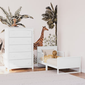 White toddler bed with guardrails angled in nursery with 5 drawer chest 