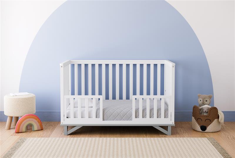 White crib with pebble gray in toddler bed conversion with two safety guardrails in nursery 