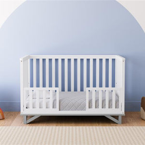White crib with pebble gray in toddler bed conversion with two safety guardrails in nursery 